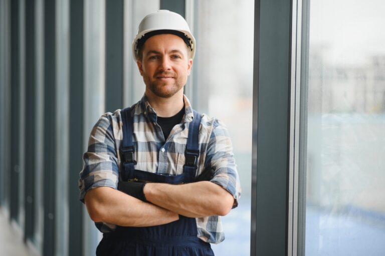 A trade worker smiles at the camera with his arms crossed.
