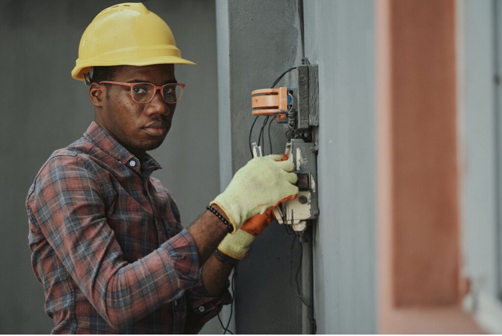 A person wearing a hard hat and gloves works on an electrical box.