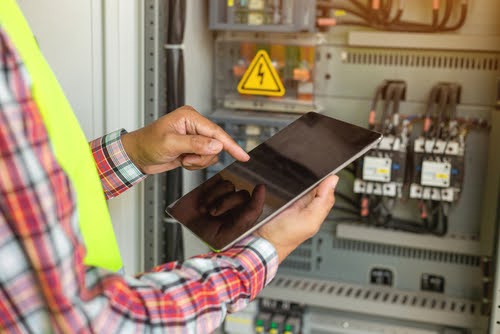 Close up hand of electrician working with tablet at factory.