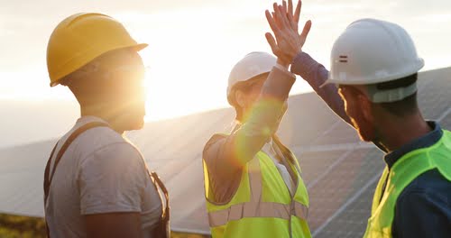 Happy employees wearing helmets and vests high-fiveing.