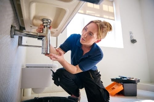 Female plumber working on sink pipes.