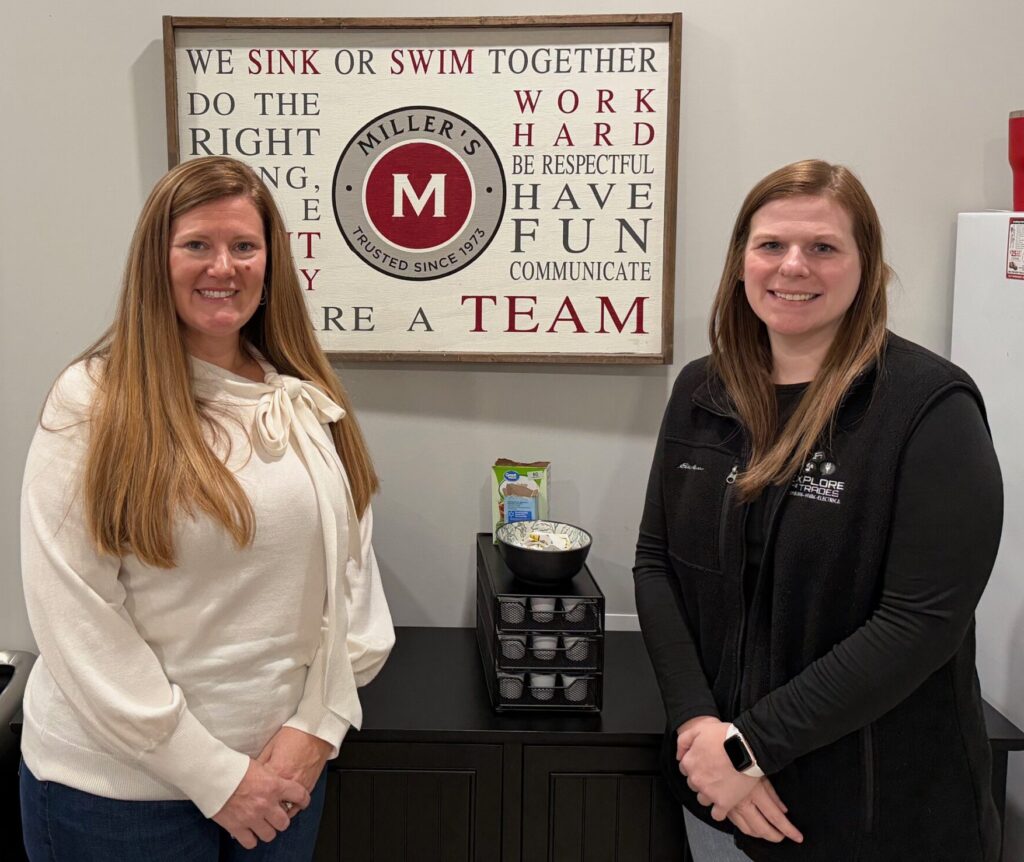 Two women standing next to a sign on the wall