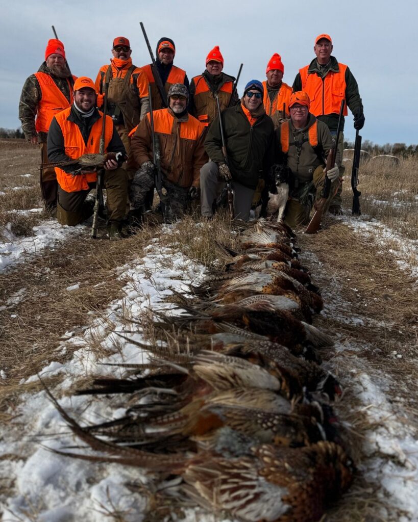 Group of men standing behind a row of shot pheasants.