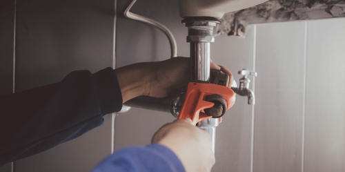 A plumber uses a wrench to fix a pipe.