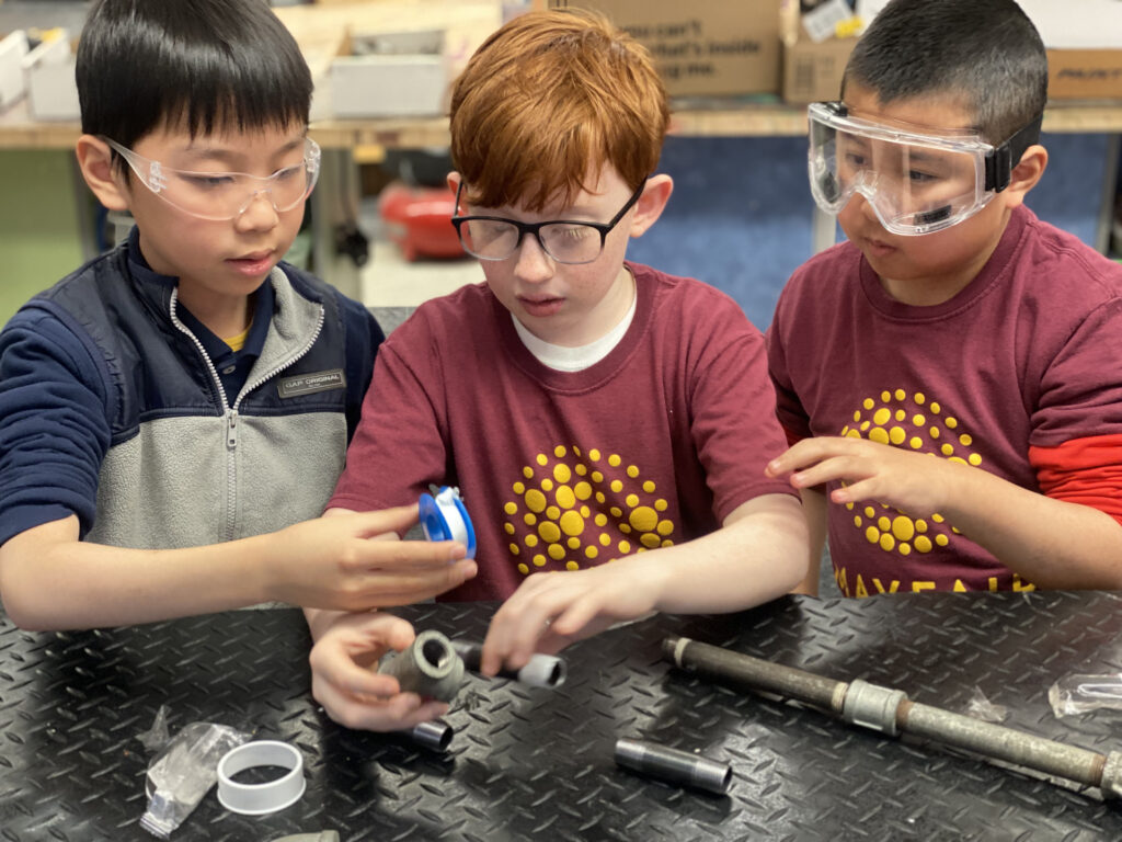Three young boys working with pipe materials.