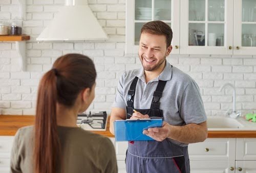Plumber talking in kitchen with customer.
