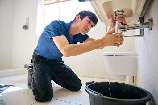 Plumber working on pipe under sink.