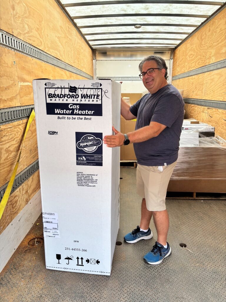 Man standing beside a boxed water heater inside a delivery truck